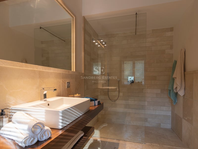 Salle de bain contemporaine avec douche en verre, pierre naturelle et vasque sur plan de travail en bois.