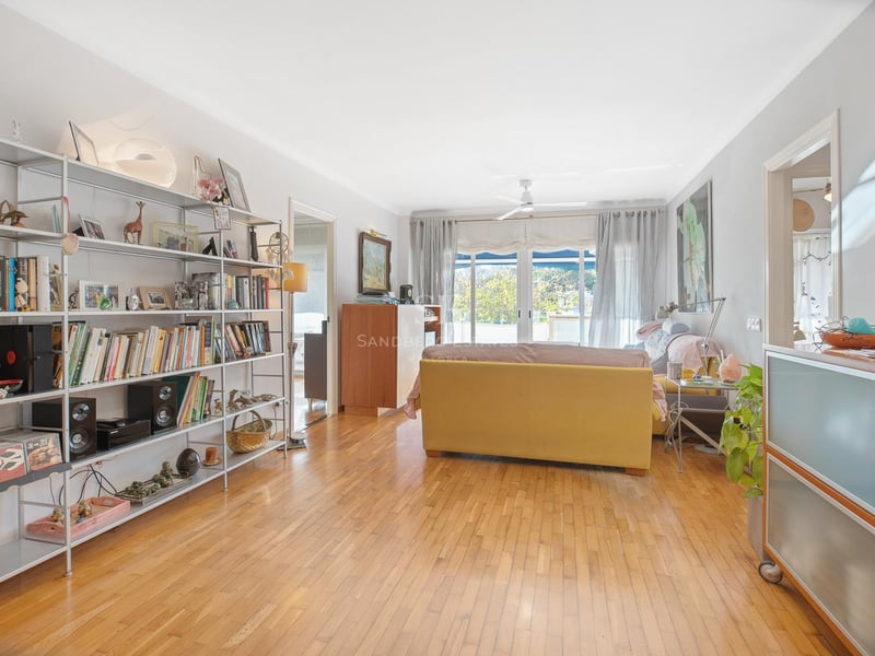 Salon spacieux avec parquet en chêne miel, grande étagère métallique et baies vitrées ouvrant sur un balcon.