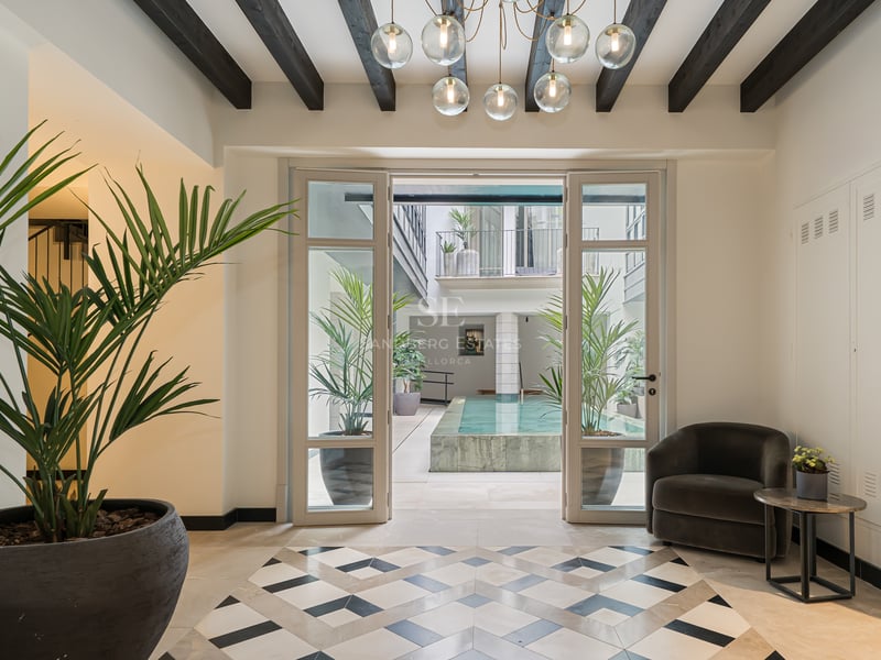 Lujoso hall de entrada con suelos geométricos que dan a un patio interior con piscina y plantas tropicales.