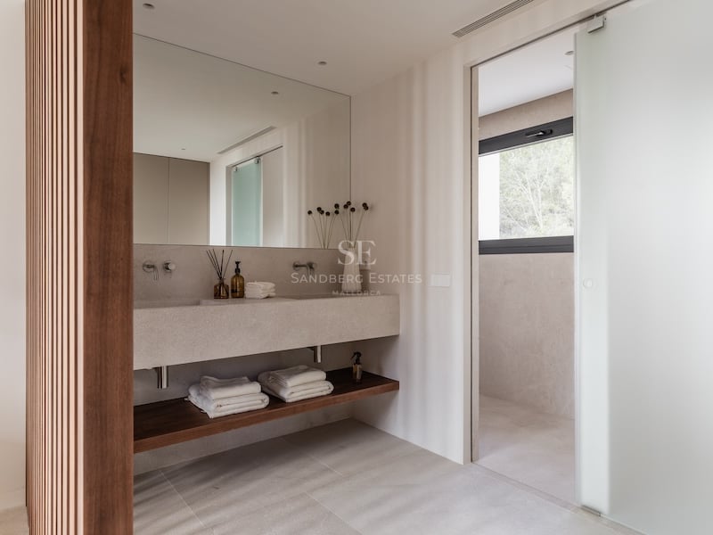 Salle de bain moderne dotée d'une double vasque en pierre beige, d'un mur en tasseaux de bois et d'une porte dépolie.