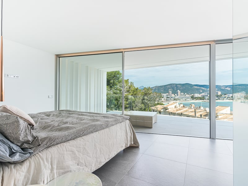 Chambre lumineuse avec grand lit et baies vitrées ouvrant sur une terrasse surplombant la côte et les montagnes.