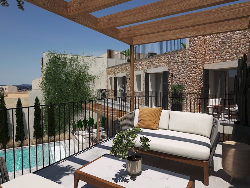Terraza moderna con pérgola de madera, sofá de diseño y pared de piedra natural con vistas a una piscina inferior.