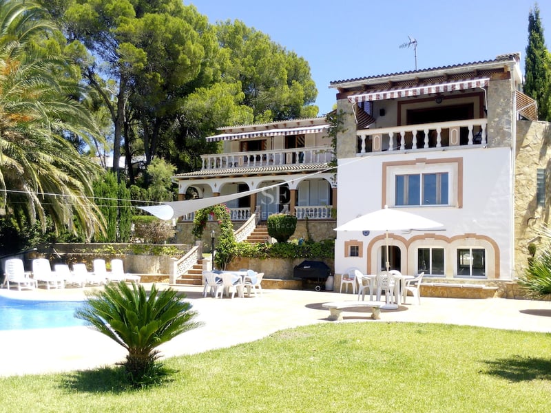 Grande villa blanche de style méditerranéen avec piscine bleue, chaises longues et végétation luxuriante.