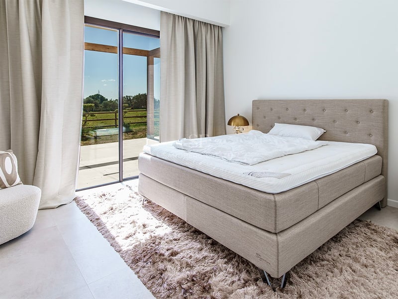 Chambre de luxe avec lit capitonné, tapis moelleux et grandes baies vitrées ouvrant sur un jardin.