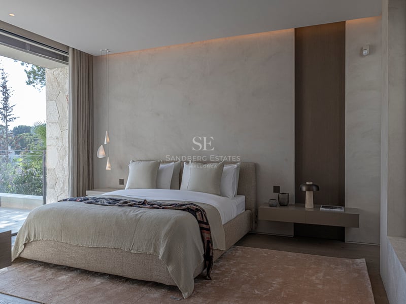 Chambre principale moderne, tons neutres, murs texturés, grandes baies vitrées donnant sur une terrasse en pierre.