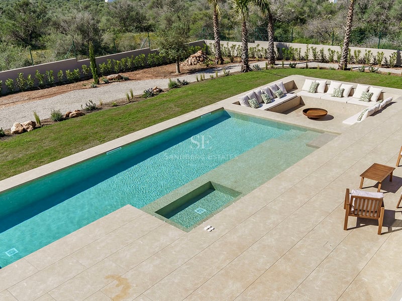Piscine rectangulaire turquoise avec terrasse en pierre naturelle et coin salon encastré avec coussins et brasero.