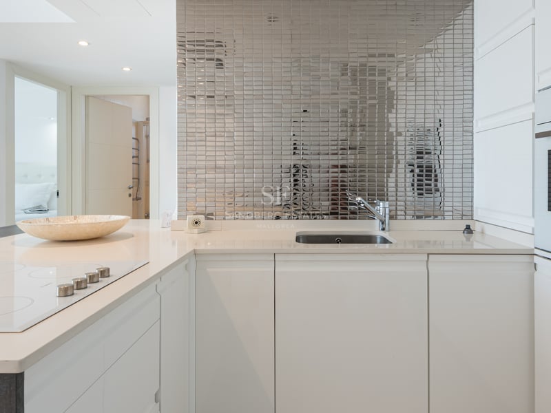 Cuisine moderne blanche avec crédence en mosaïque de miroir, plan de travail en quartz et four encastré.