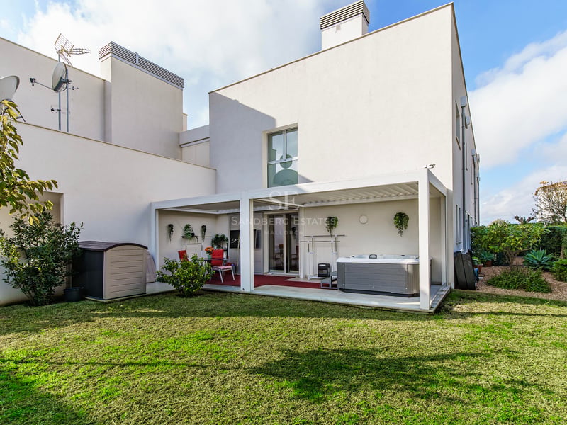 Un bâtiment blanc moderne avec une pelouse verte et une terrasse couverte comprenant un jacuzzi et un coin repas.