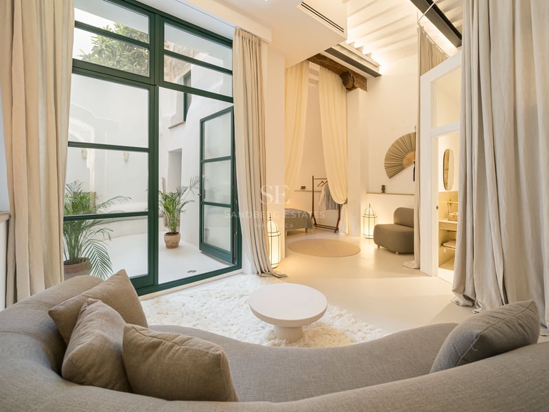 Salon moderne avec un grand canapé incurvé, un tapis à poils longs et des baies vitrées ouvrant sur un patio blanc.