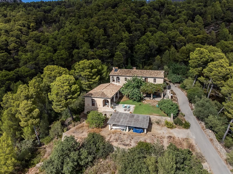 Vue d'oiseau d'une villa rustique avec toits en terre cuite entourée d'une forêt de pins dense sur une colline.