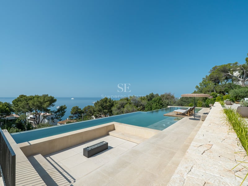 Vue en plongée d'une piscine à débordement de luxe et d'un coin salon avec brasero surplombant la Méditerranée.