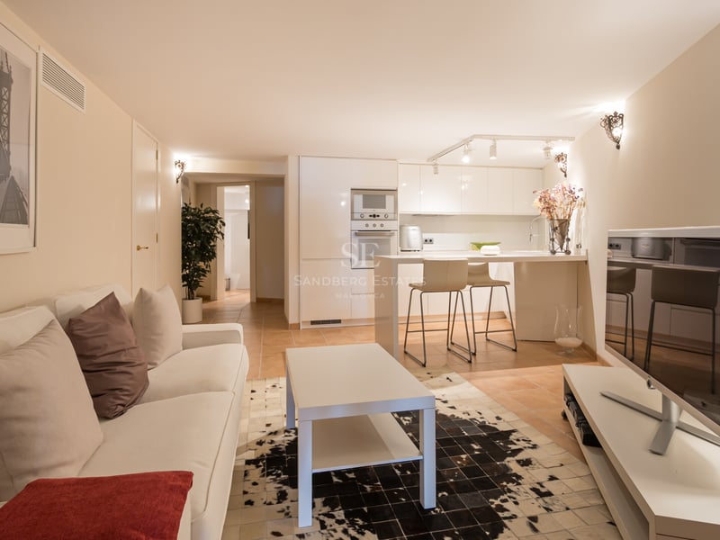 Salon moderne à aire ouverte avec canapé blanc, tapis en peau de vache et cuisine intégrée blanche avec comptoir.