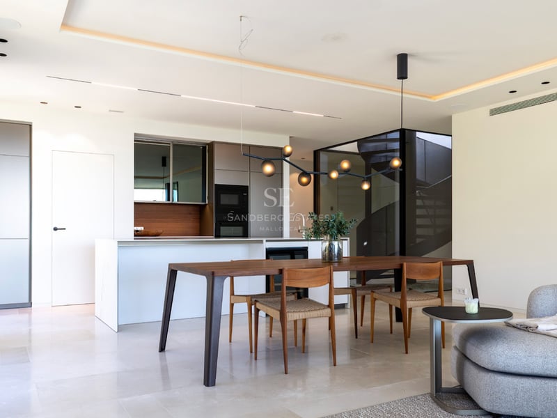 Salle à manger à aire ouverte avec table en noyer, îlot de cuisine blanc et éclairage contemporain dans une villa.