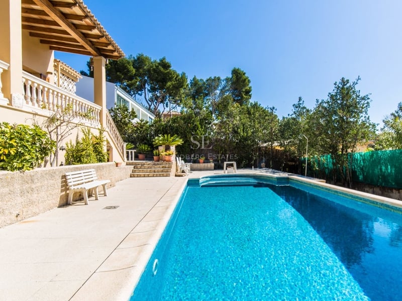 Une grande piscine rectangulaire bleue à côté d'une villa de style méditerranéen avec terrasse en pierre et verdure.
