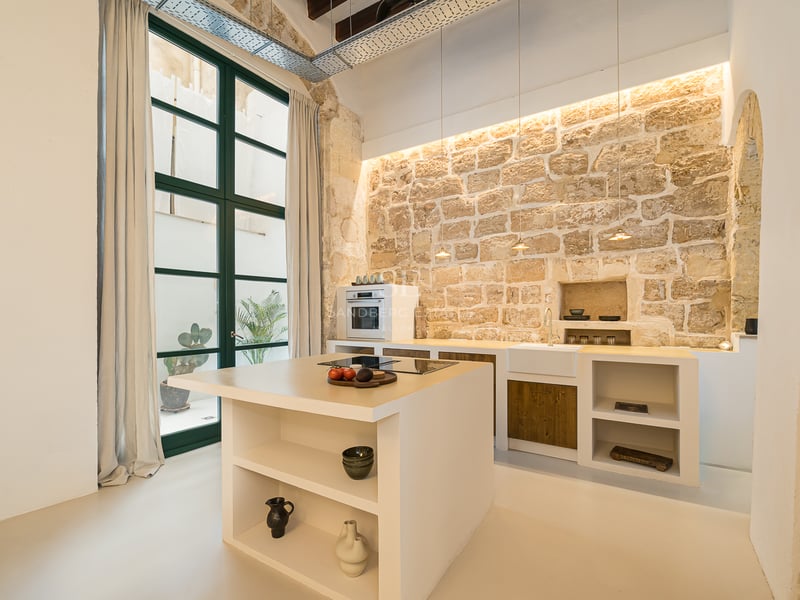 Cuisine design avec îlot blanc, mur en pierre apparente et une grande fenêtre industrielle.