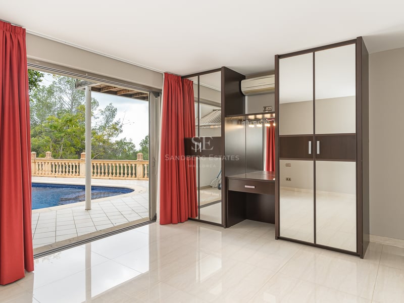 Chambre moderne avec rideaux rouges, armoires à miroirs et coiffeuse, donnant sur une piscine via des baies vitrées.