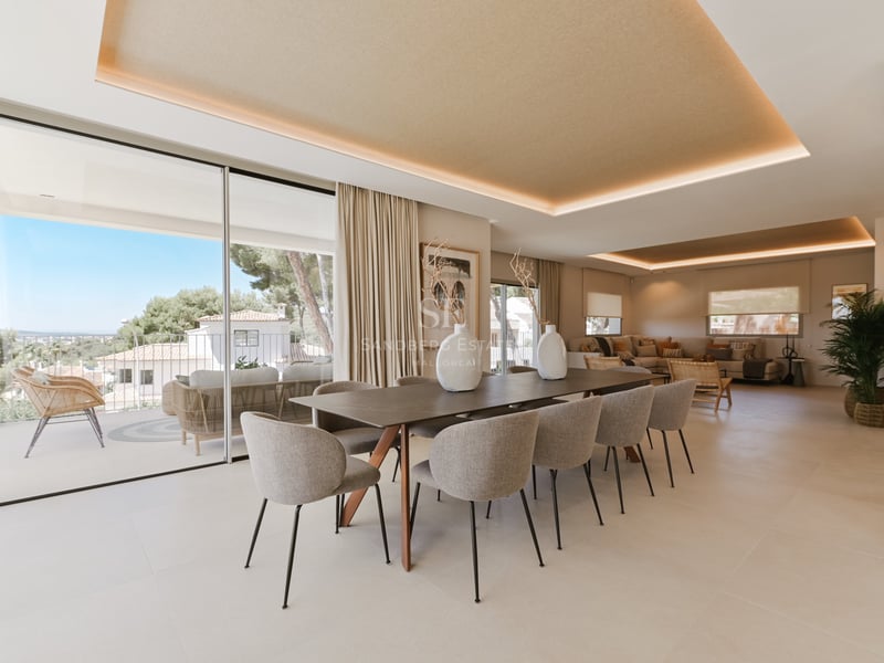 Salle à manger minimaliste avec table en bois, chaises en velours gris et grandes baies vitrées coulissantes.