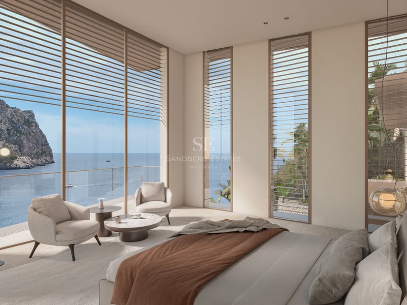 Chambre moderne avec baies vitrées donnant sur l'océan, fauteuils beiges et décoration épurée.