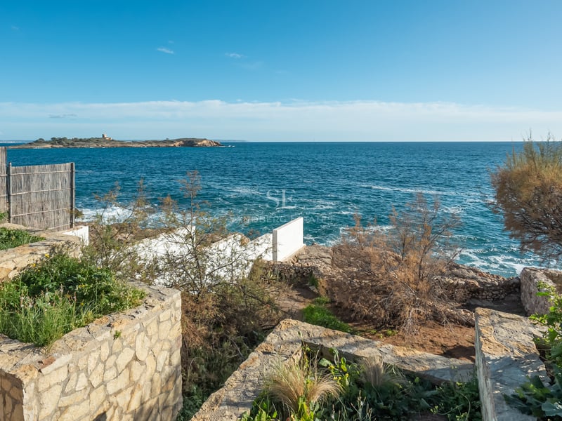 Terrasse en pierre naturelle surplombant une mer d'un bleu profond avec une petite île à l'horizon sous un ciel clair.