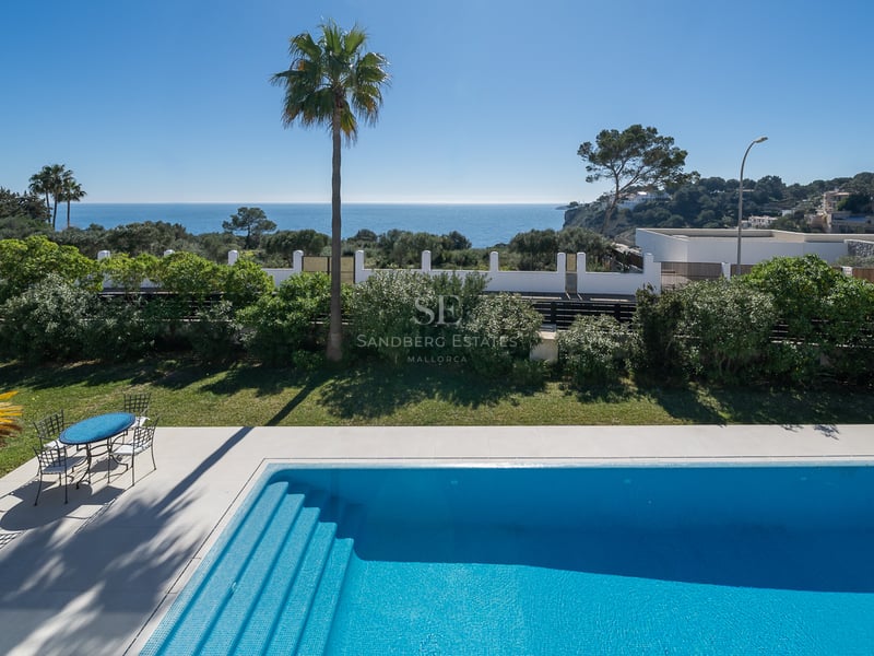 Piscine bleue entourée d'un jardin avec vue directe sur la Méditerranée sous un ciel clair.