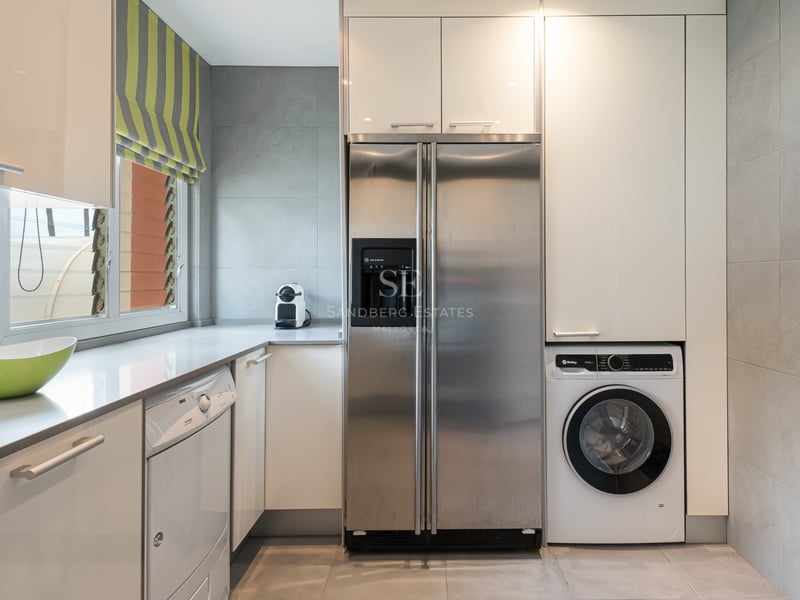 Espace buanderie avec réfrigérateur américain en inox, lave-linge et placards blancs sur carrelage gris.