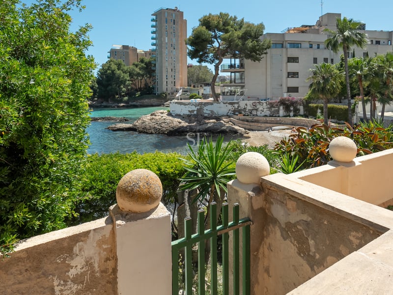 Vue d'une baie aux eaux turquoise et d'un rivage rocheux depuis une terrasse méditerranéenne en pierre.