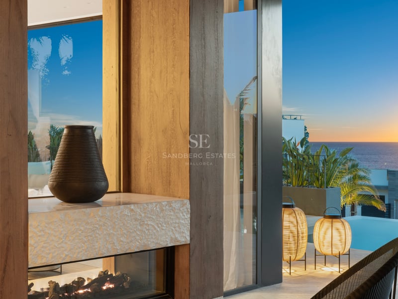 Terrasse de luxe au coucher du soleil avec cheminée vitrée, boiseries en chêne, mobilier design et vue sur la piscine.
