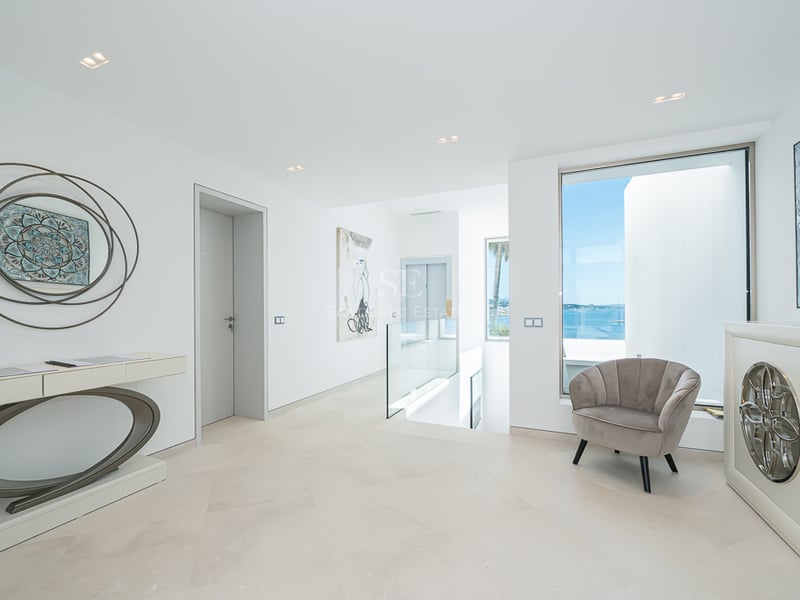 Couloir moderne et lumineux avec sols en pierre, rampes en verre, ascenseur et grande fenêtre sur la mer bleue.