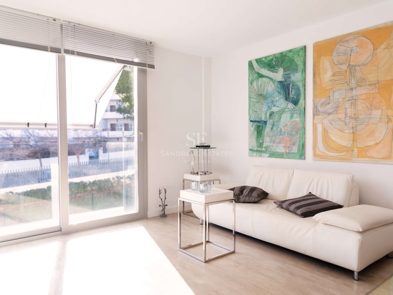 Salon lumineux avec canapé en cuir blanc, deux grands tableaux abstraits et baies vitrées toute hauteur.