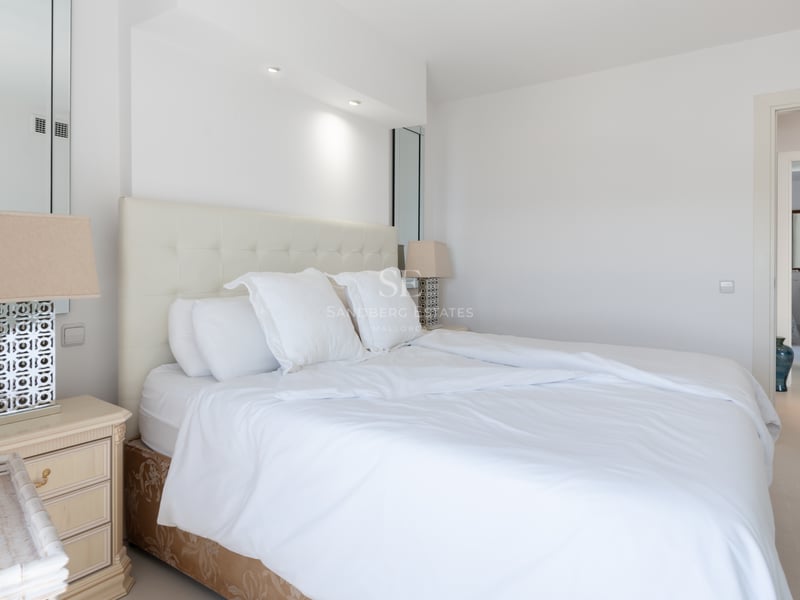 Chambre lumineuse avec tête de lit capitonnée blanche, tables de chevet symétriques et sol en carrelage clair.