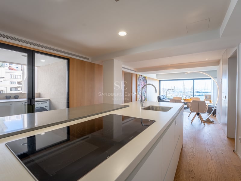 Îlot de cuisine avec plaque à induction et évier, ouvrant sur une salle à manger et le port en arrière-plan.