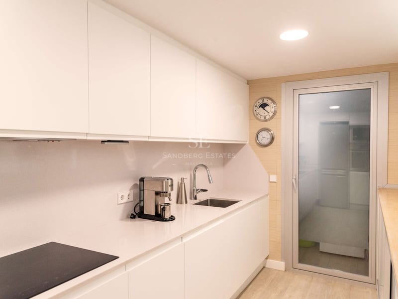 Cuisine moderne blanche avec placards sans poignées, plan de travail en quartz et porte vitrée.