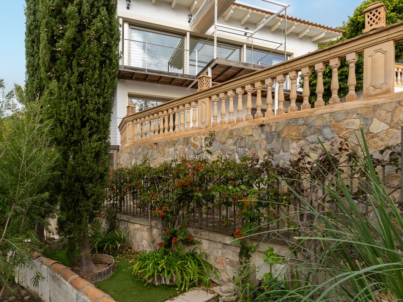 Jardin en terrasses avec murs en pierre, balustrades classiques et cyprès devant une villa blanche.