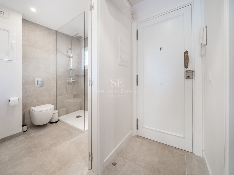 Salle de bains contemporaine avec douche vitrée, toilettes suspendues et carrelage en grès cérame tons sable.