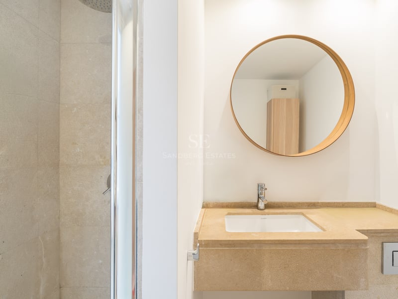 Salle de bain contemporaine avec vasque en pierre beige, miroir rond en bois et douche à l'italienne vitrée.