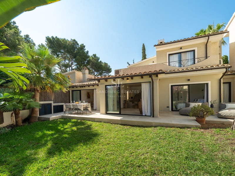 Vue extérieure d'une villa crème avec toit en terre cuite, pelouse et grandes baies vitrées coulissantes.