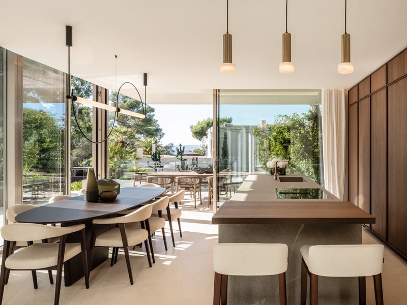 Cuisine de luxe avec îlot en pierre, menuiserie en noyer et salle à manger ouvrant sur une terrasse ensoleillée.
