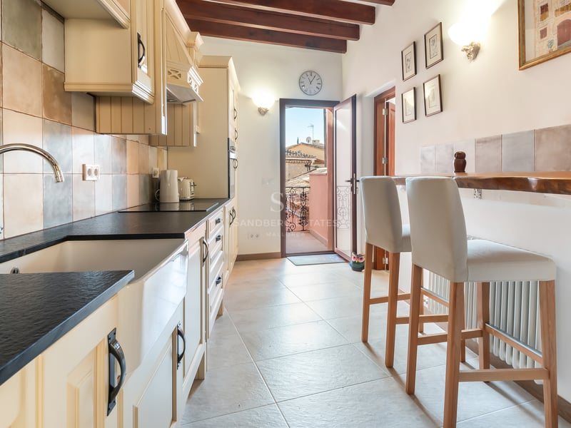 Cuisine avec plan de travail sombre, évier de ferme, poutres en bois et accès à une terrasse ensoleillée.