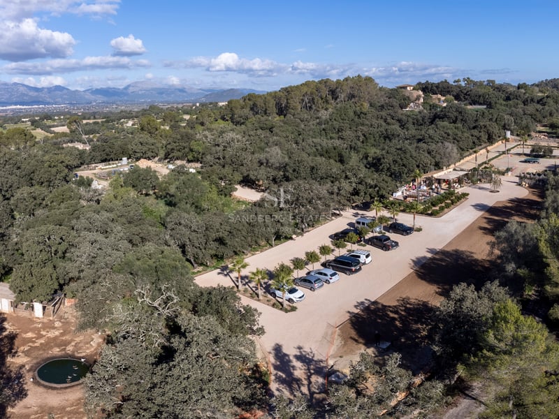Vue aérienne par drone d'un grand domaine méditerranéen avec parking, entouré d'une forêt dense et de montagnes.