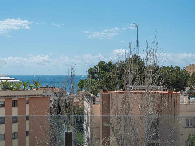 Vue de la mer Méditerranée et des bâtiments côtiers à travers un garde-corps en verre sous un ciel bleu.