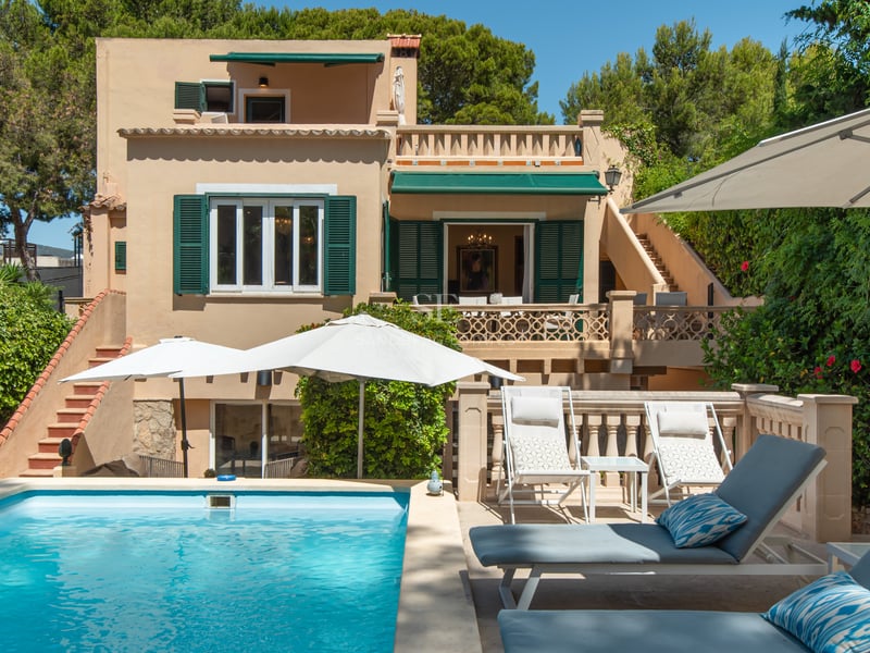 Vue extérieure d'une villa avec piscine turquoise, chaises longues et façade ocre aux volets verts.