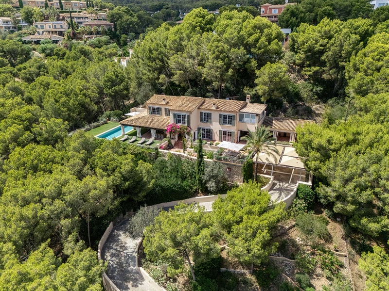 Vue aérienne d'une villa méditerranéenne avec piscine et toit en terre cuite entourée d'une forêt dense.