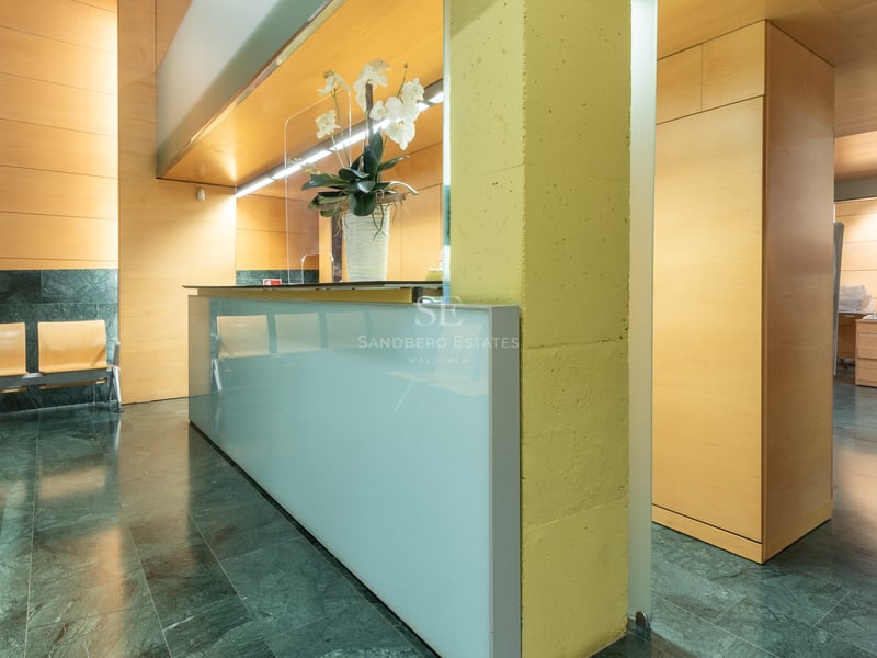 Modern lobby featuring a frosted glass reception desk, green marble floors, and light wood wall panels.