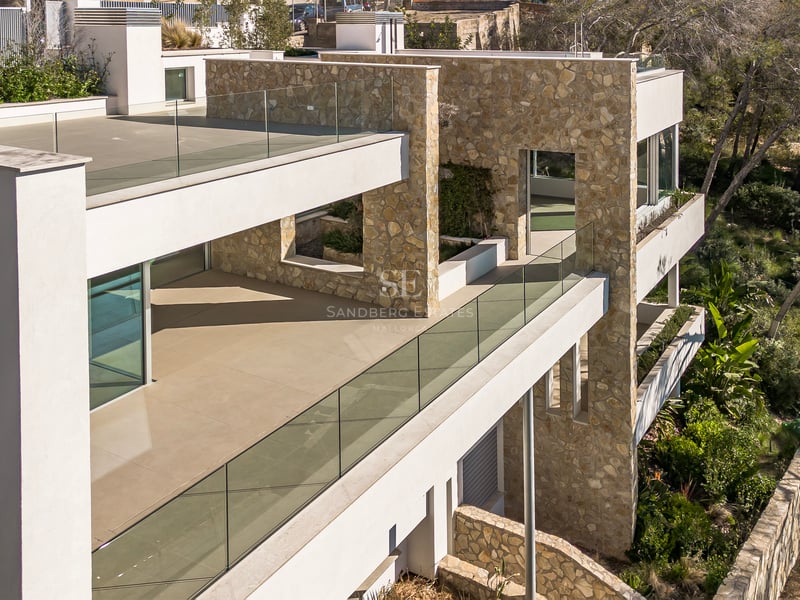 Villa contemporaine à plusieurs étages avec murs en pierre naturelle, garde-corps en verre et vastes terrasses.