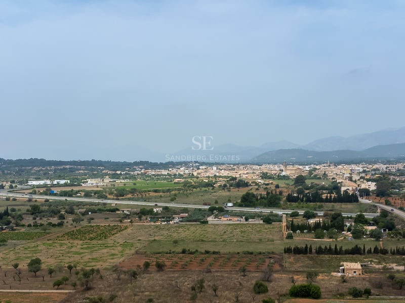 Vaste paysage d'un village majorquin entouré de champs agricoles et de montagnes sous un ciel voilé.