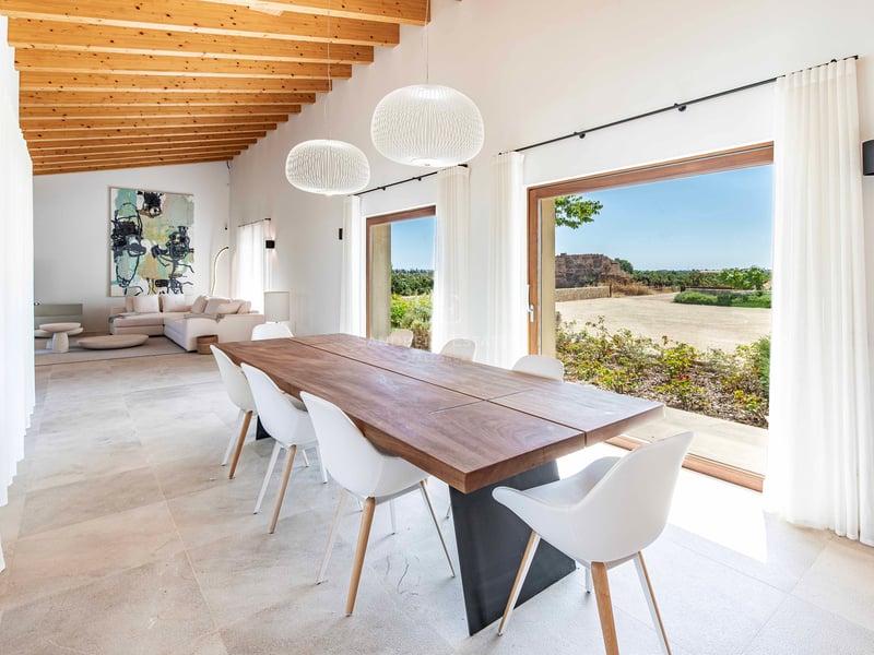 Intérieur d'une salle à manger lumineuse avec table en bois, chaises blanches et plafond à poutres.
