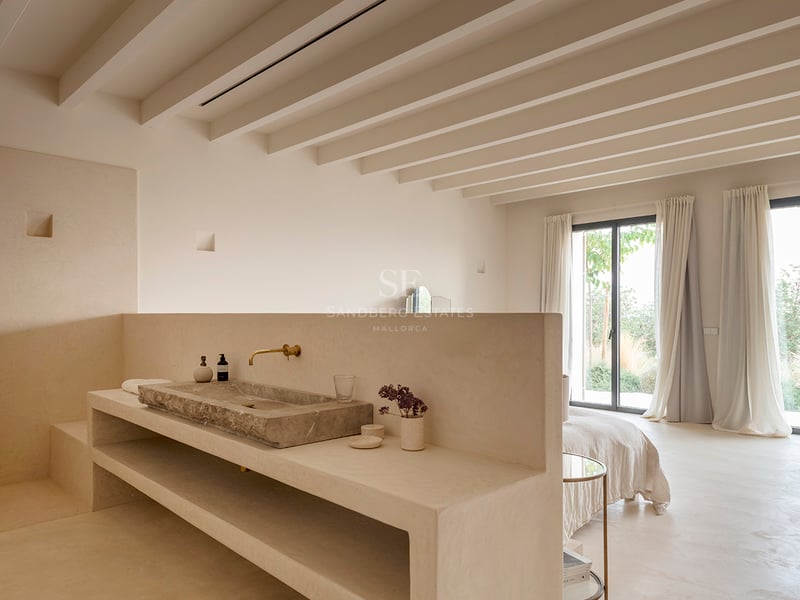 Minimalist bedroom with a built-in stone washbasin, exposed ceiling beams, and floor-to-ceiling glass doors.