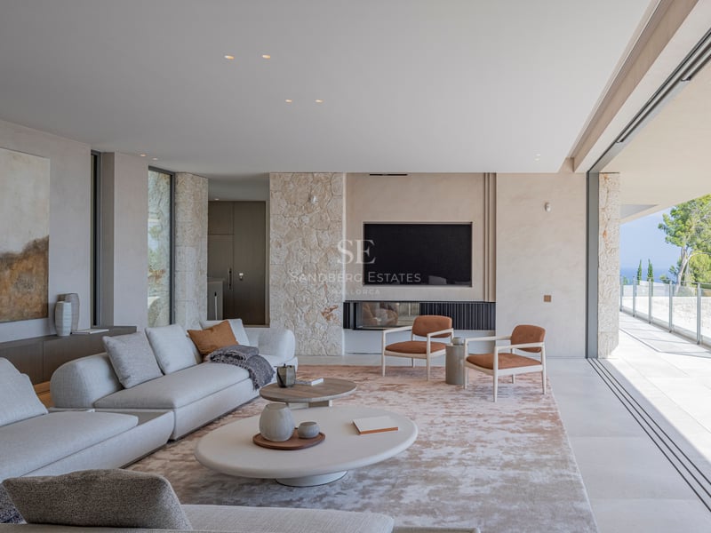 Salon minimaliste avec murs en pierre, canapé gris et baies vitrées coulissantes ouvrant sur une terrasse.