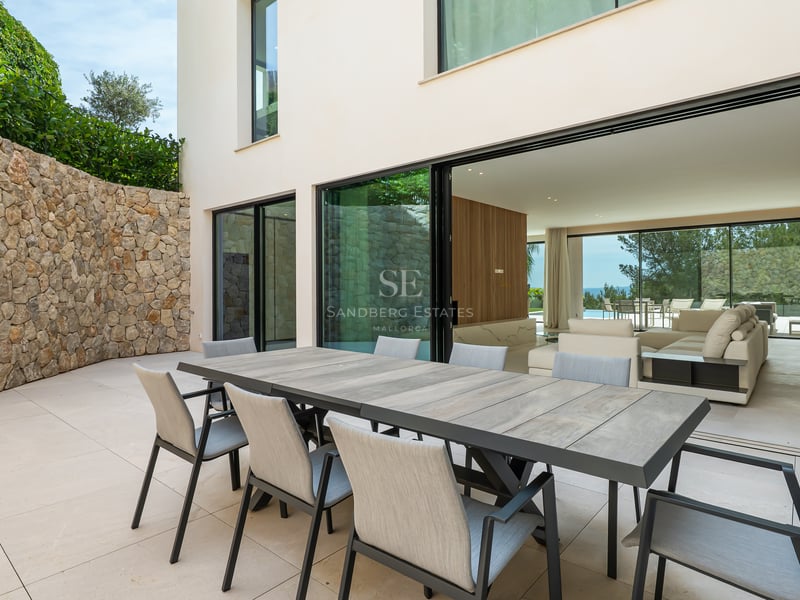 Table à manger d'extérieur sur une terrasse en pierre avec mur en pierre naturelle et baies vitrées coulissantes.