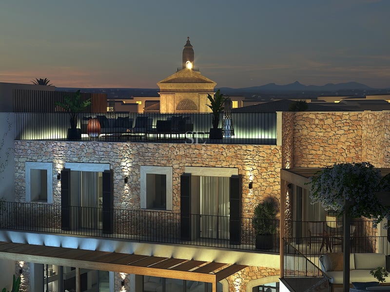 Vista nocturna de una villa mediterránea con paredes de piedra iluminadas y terraza en la azotea con vistas al pueblo.